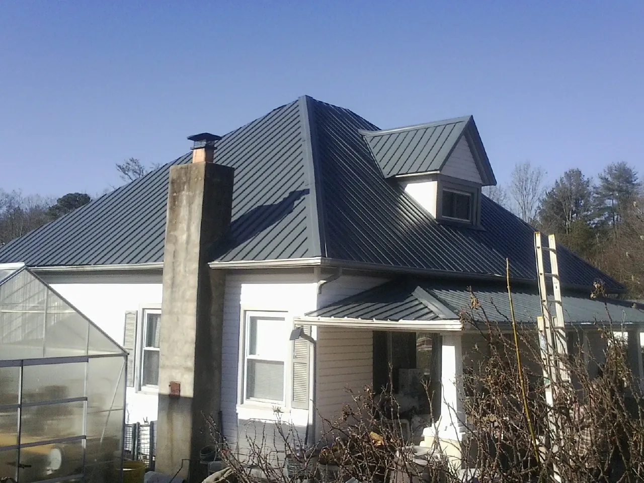 Dark blue standing seam metal roof on a white farmhouse with dormer — Slate & Tile Roof Repair by Roofing Brothers in Villard