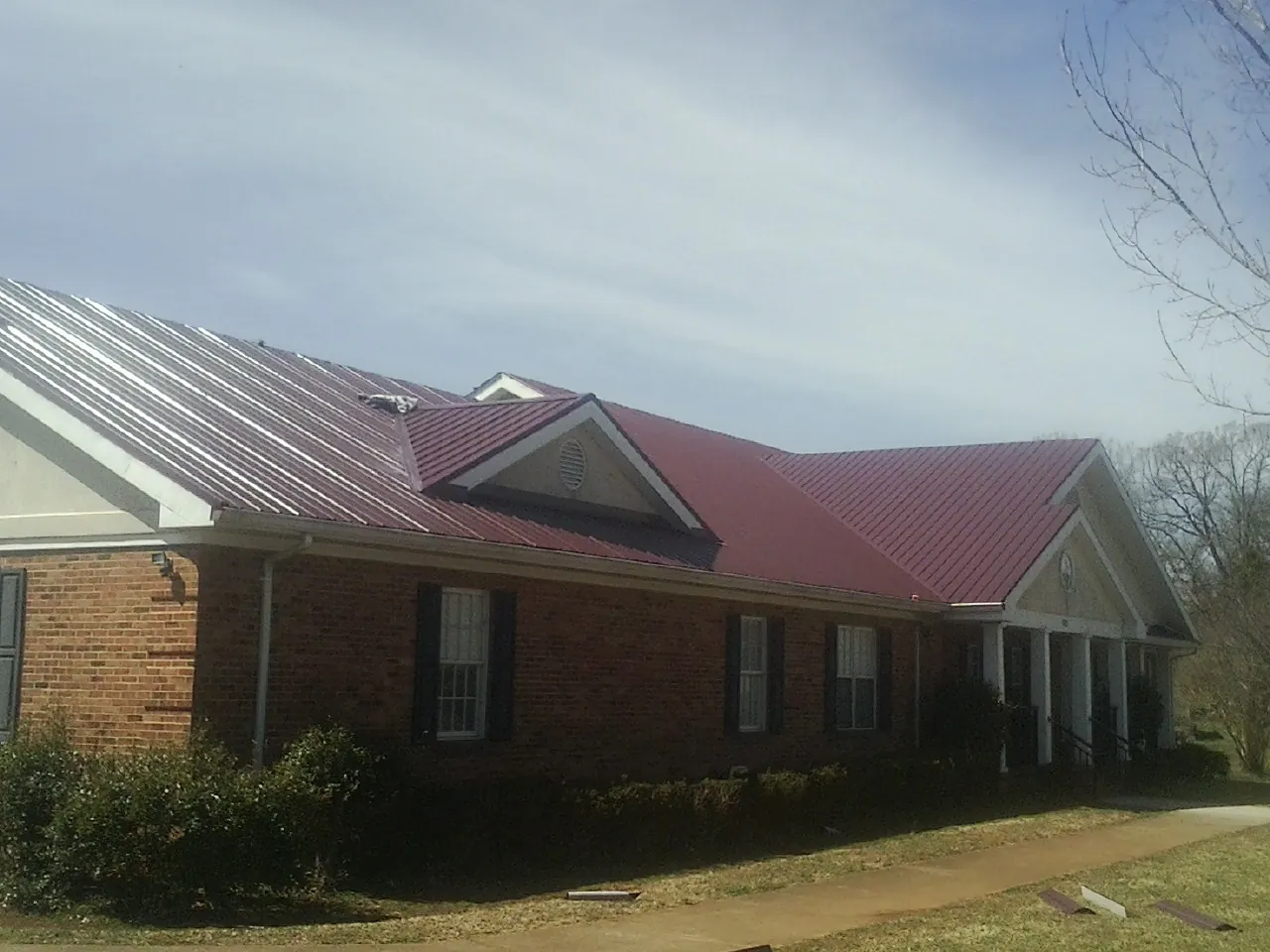 Red metal roof with gabled entries on a long brick building, from a Hail Damage Roof Repair job in Villard