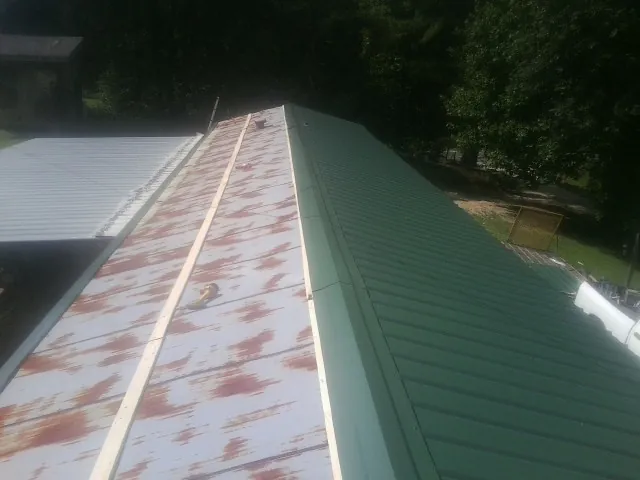 Old rusted panels beside newly installed green metal roofing — Wind Damage Roof Repair by Roofing Brothers in Villard