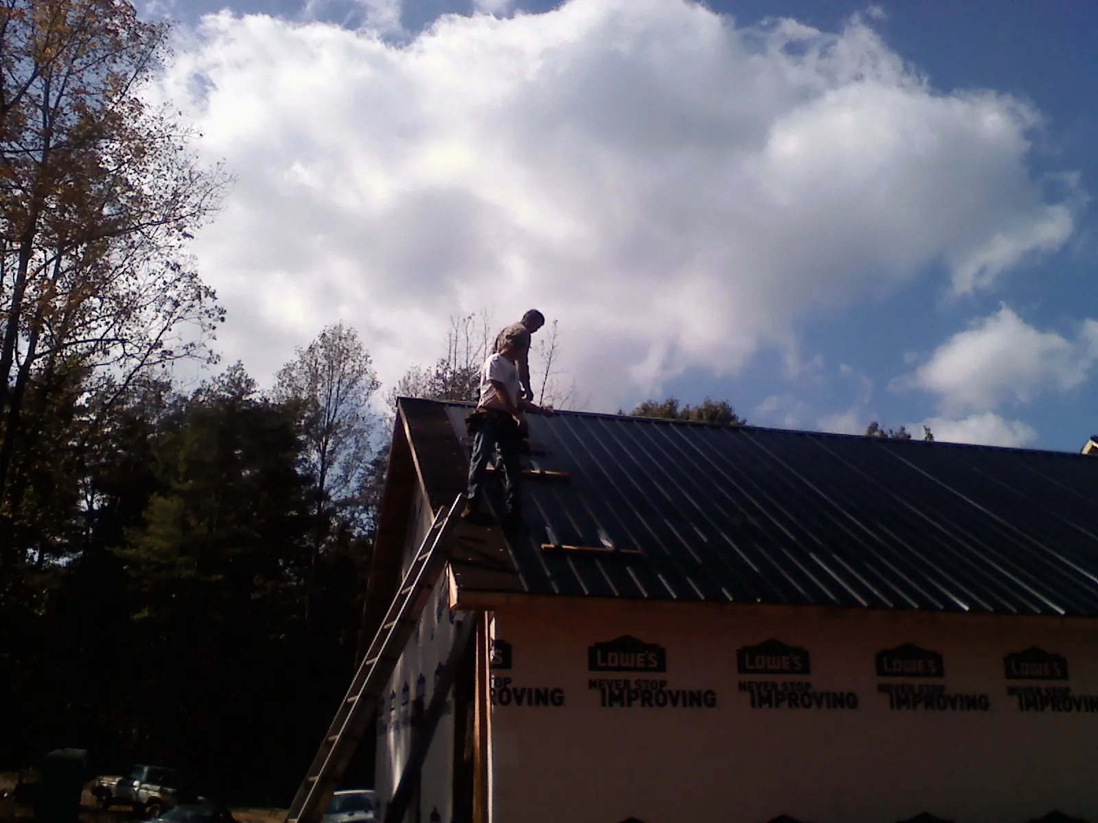 Roofer fastening dark metal panels high against a cloudy sky, from a Roof Inspection job in Villard