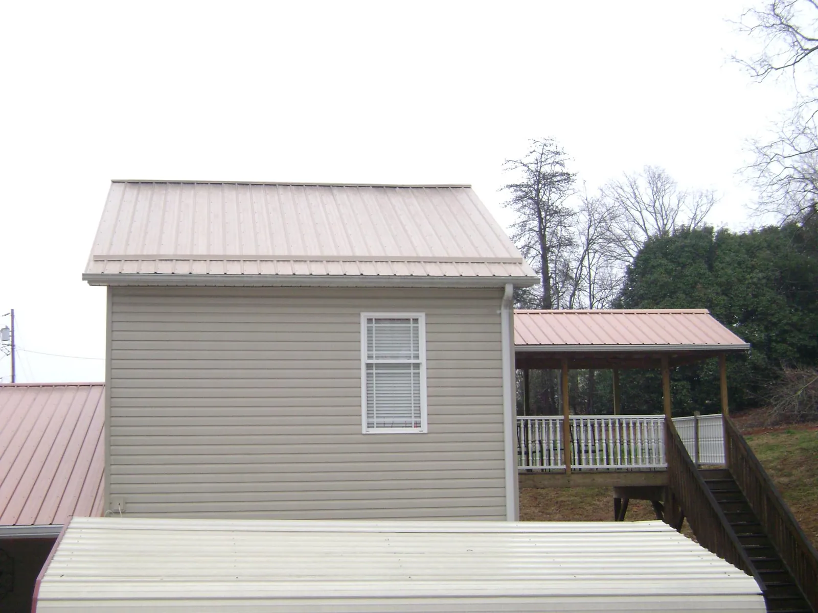 Tan metal roofs on a two story addition and attached porch, from a Roof Replacement job in Villard